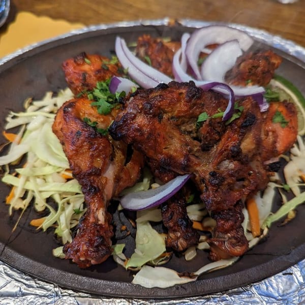 Sizzling Indian chicken tikka with onions and cabbage on a dark platter.