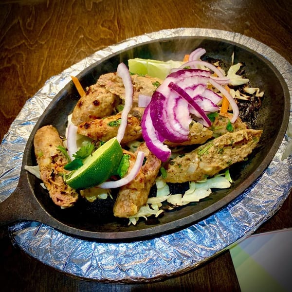 Sizzling Indian seekh kebabs with red onions, lime, and cabbage on a cast iron platter.
