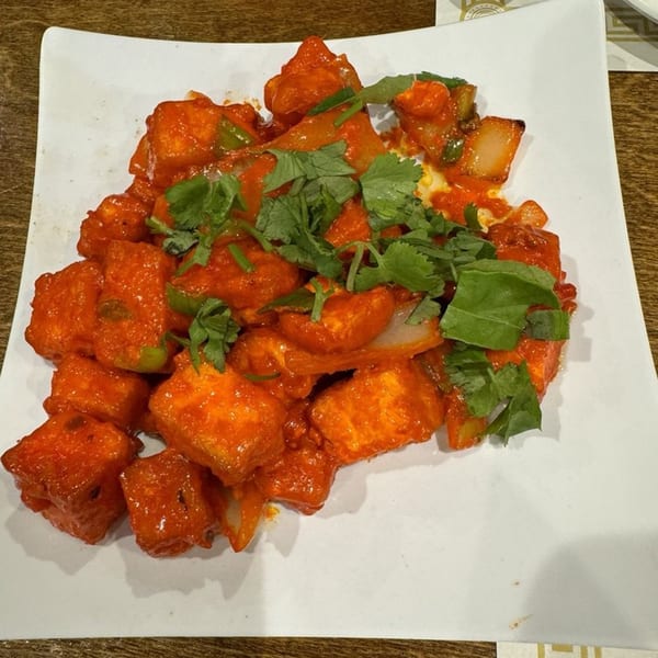 Indian chili paneer, a vibrant red dish with green peppers and cilantro, on a white plate.