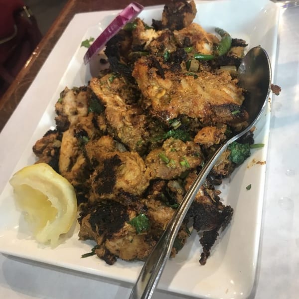 A white rectangular plate of Daawath Indian Cuisine's chicken tikka, garnished with lemon and red onion.
